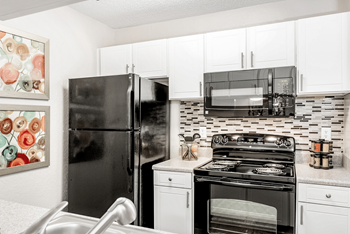 A black refrigerator stands in a kitchen with white cabinets and a black stove at Paces Pointe Apartment Homes, Matthews, 28105